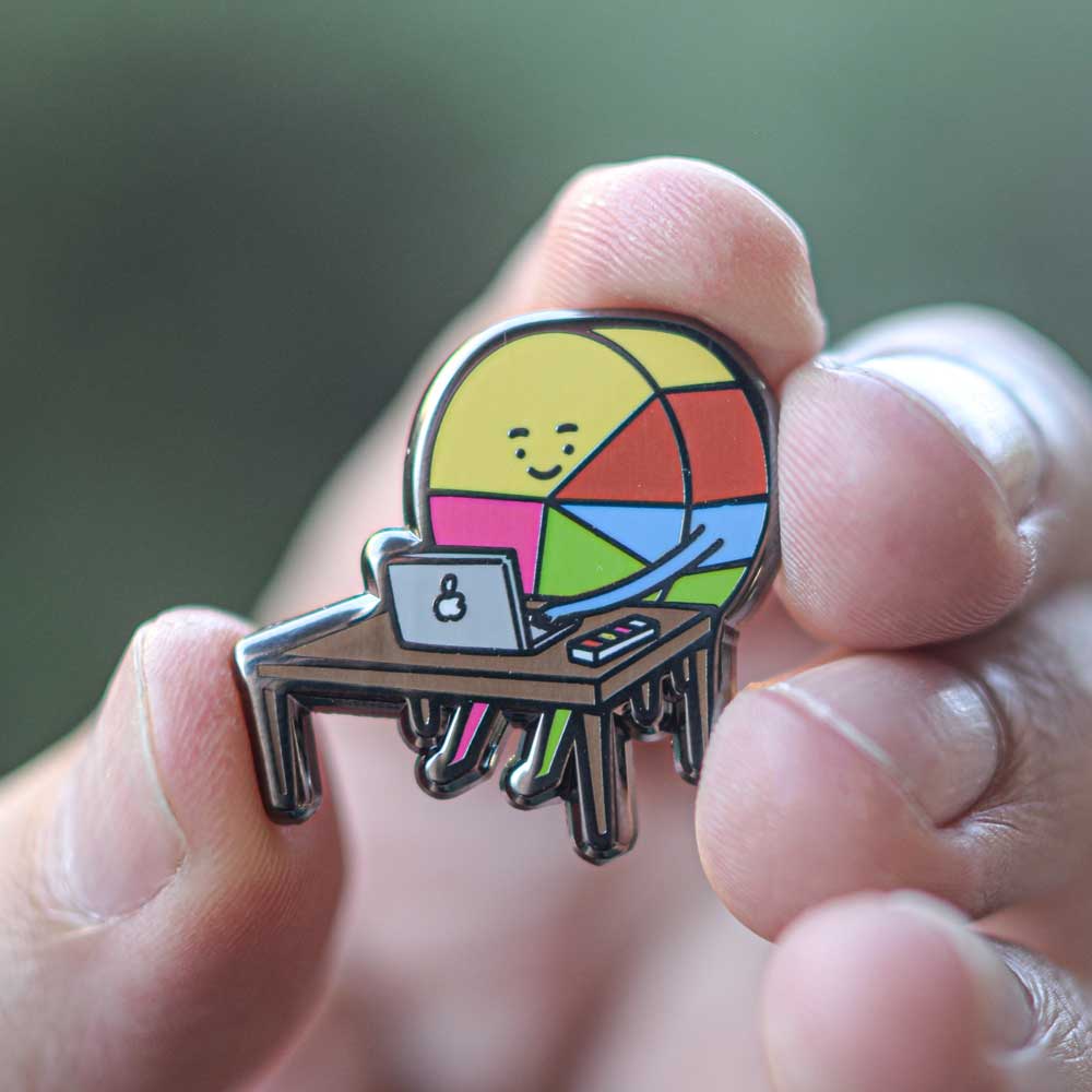 Pin ilustrado de Ingesman sostenido en la mano, muestra su tamaño y detalle del diseño